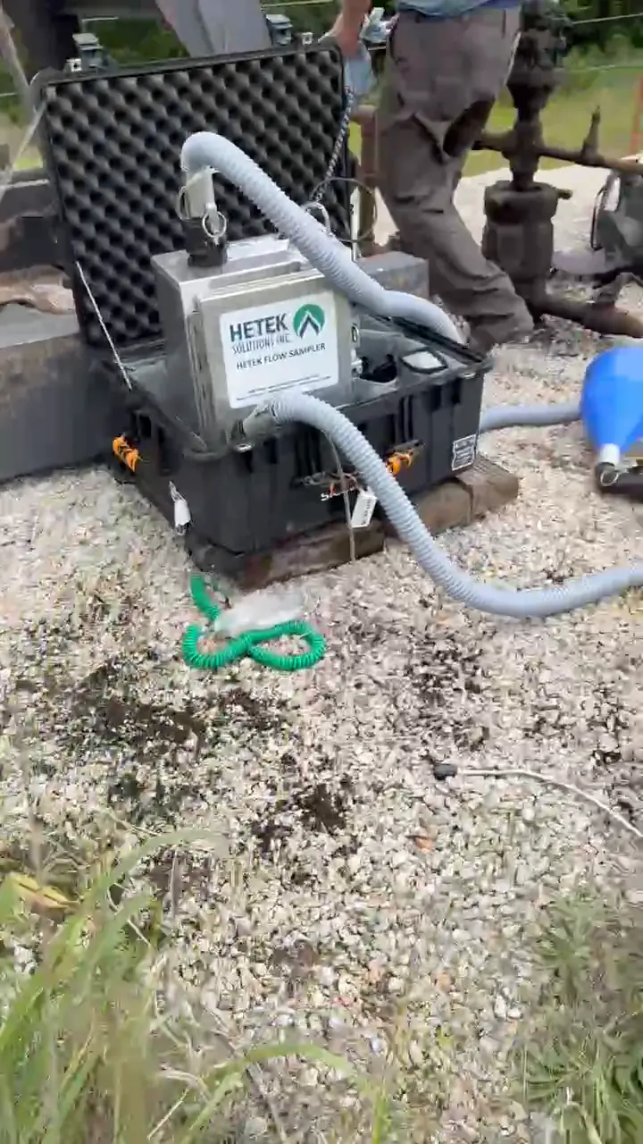 A Hi-Flow sampler in an open case on a gravel well pad, its hoses running to a capture hood at the wellhead.