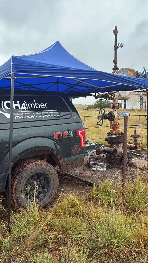 A CH4mber survey truck under a blue canopy beside a rusted wellhead in a fenced pad