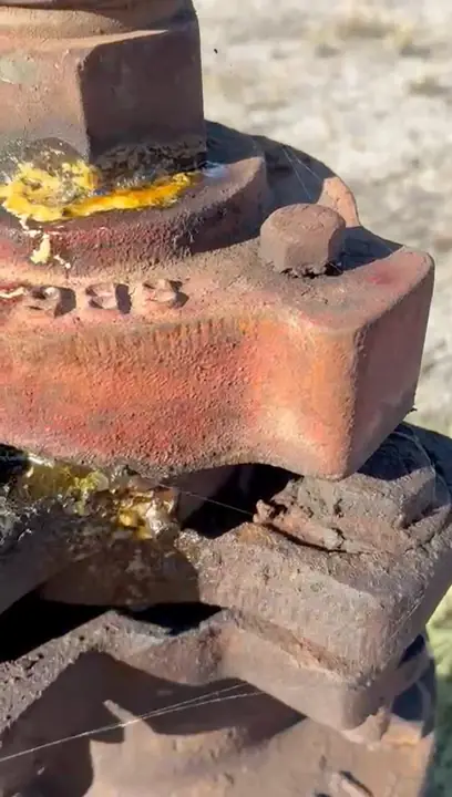 Close-up of a rusted, corroded wellhead flange on an old orphaned well, with fluid bubbling at the joint